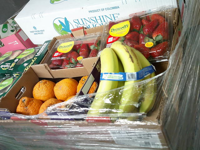 Two calmshell cases of strawberries, oranges, and bananas in a fruit box surrounded by wrap plastic..
